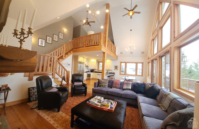 living room featuring a towering ceiling, ceiling fan with notable chandelier, and light hardwood / wood-style flooring