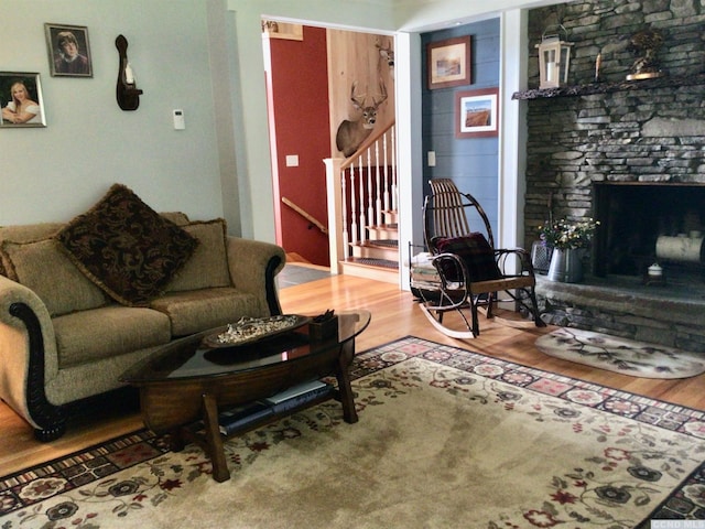 living area with a stone fireplace, stairway, and wood finished floors