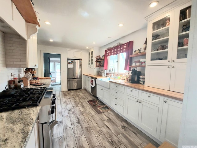 kitchen featuring appliances with stainless steel finishes, wood finish floors, white cabinetry, and a sink