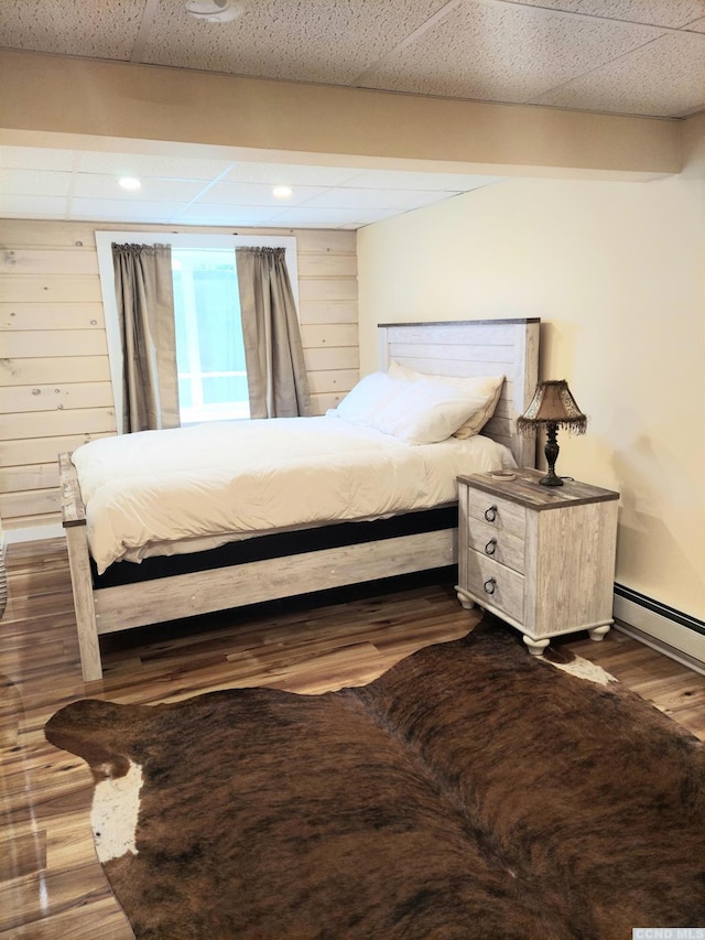 bedroom with a drop ceiling, wood finished floors, and wooden walls