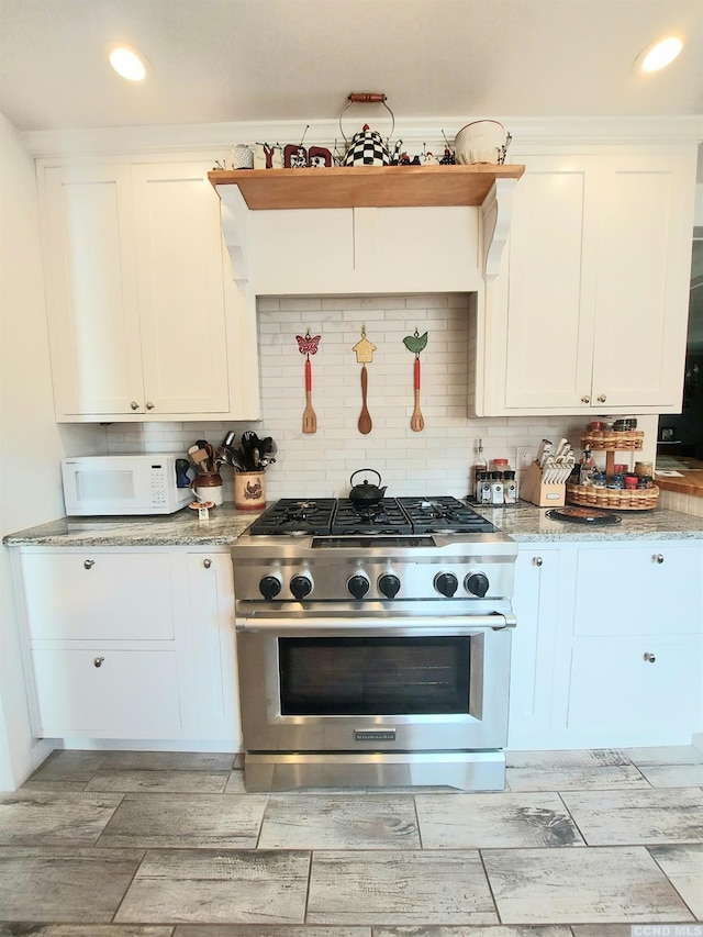 kitchen featuring white microwave, white cabinetry, high end range, and backsplash