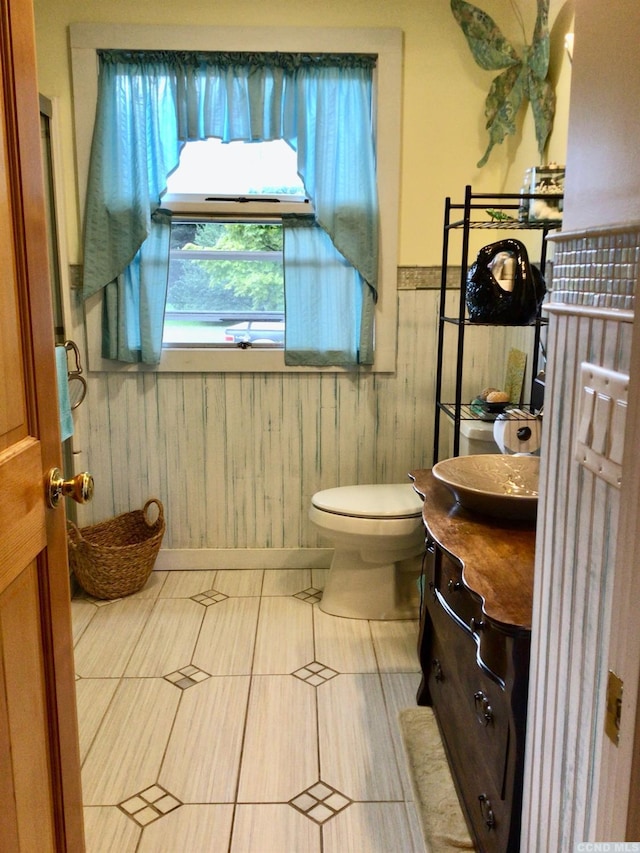 bathroom with toilet, wooden walls, vanity, wainscoting, and tile patterned floors