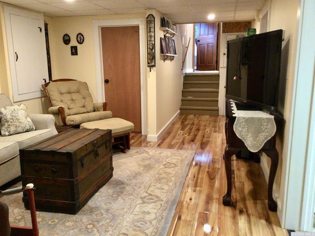 living area featuring stairs, light wood-type flooring, a paneled ceiling, and baseboards