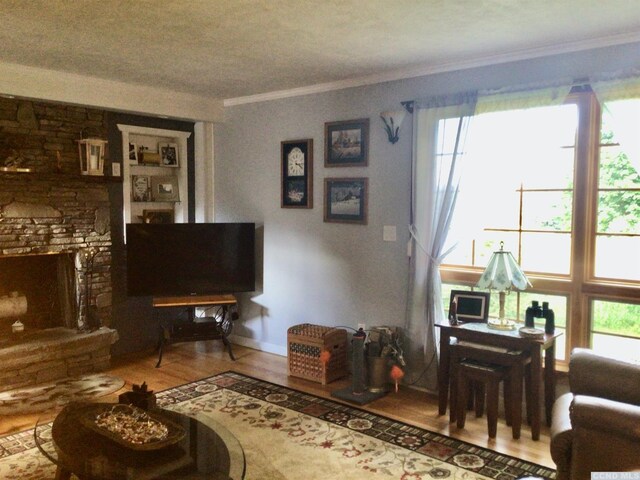 living area with a fireplace with raised hearth, baseboards, wood finished floors, and crown molding