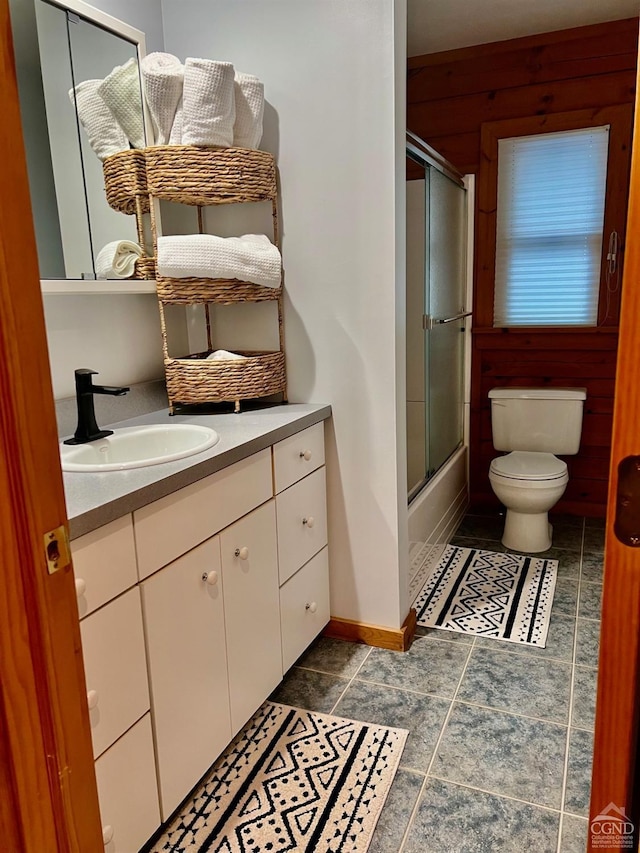 bathroom with shower / bath combination with glass door, vanity, toilet, and baseboards