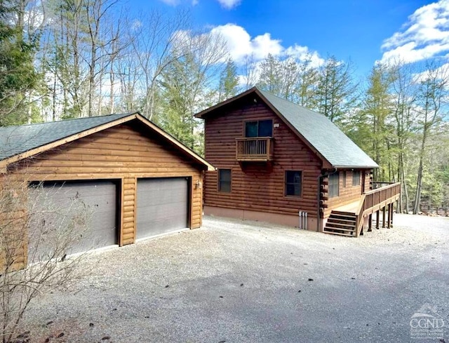 exterior space with a deck, a detached garage, log siding, and an outdoor structure