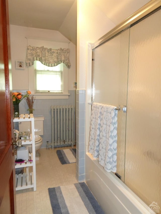 bathroom with radiator, lofted ceiling, combined bath / shower with glass door, toilet, and tile walls