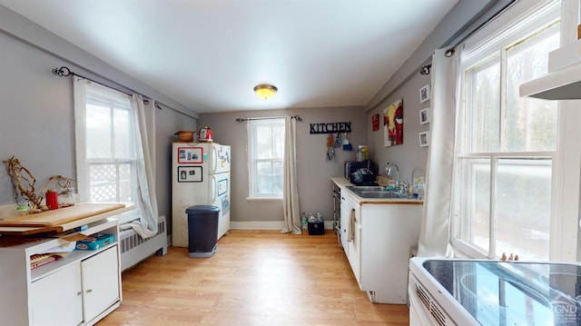 kitchen with a healthy amount of sunlight, radiator, sink, and white cabinets