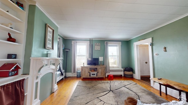 living room featuring ornamental molding, radiator, light wood-type flooring, and built in shelves