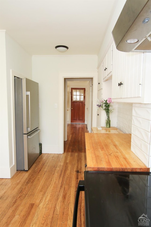 kitchen featuring white cabinets, light hardwood / wood-style floors, ventilation hood, and stainless steel refrigerator