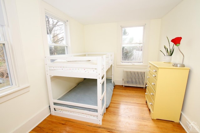 bedroom with radiator heating unit, light hardwood / wood-style flooring, and multiple windows