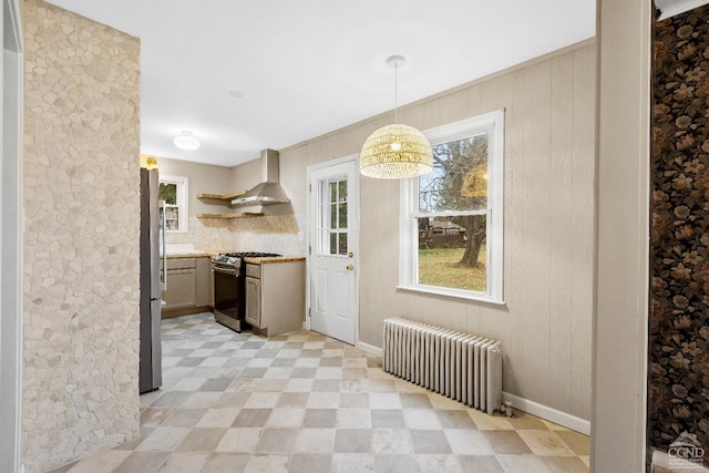 kitchen featuring radiator heating unit, wall chimney exhaust hood, an inviting chandelier, pendant lighting, and appliances with stainless steel finishes