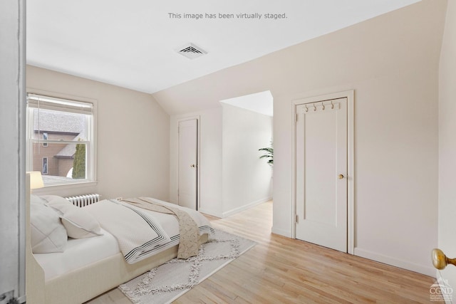 bedroom with light hardwood / wood-style floors, vaulted ceiling, and radiator