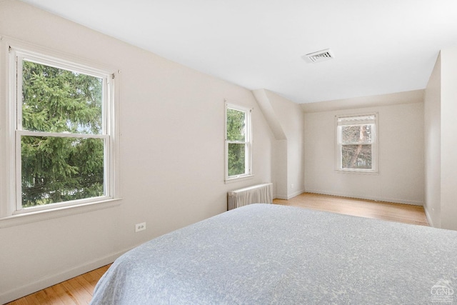 bedroom with multiple windows, radiator heating unit, and light wood-type flooring