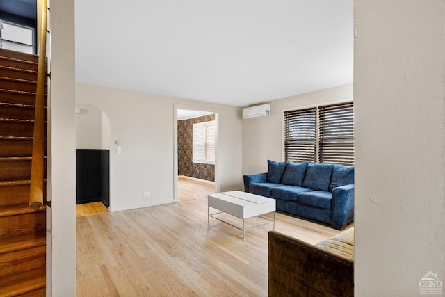 living area with stairway, light wood-type flooring, an AC wall unit, baseboards, and arched walkways
