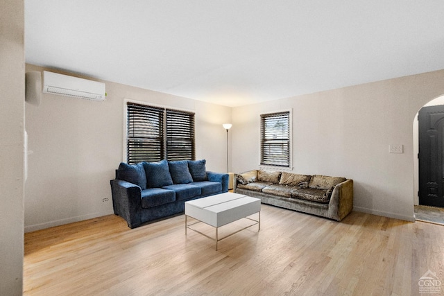 living room with baseboards, arched walkways, wood finished floors, and a wall mounted air conditioner