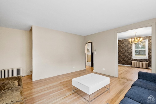 unfurnished living room featuring an inviting chandelier, light wood-style floors, radiator, and arched walkways
