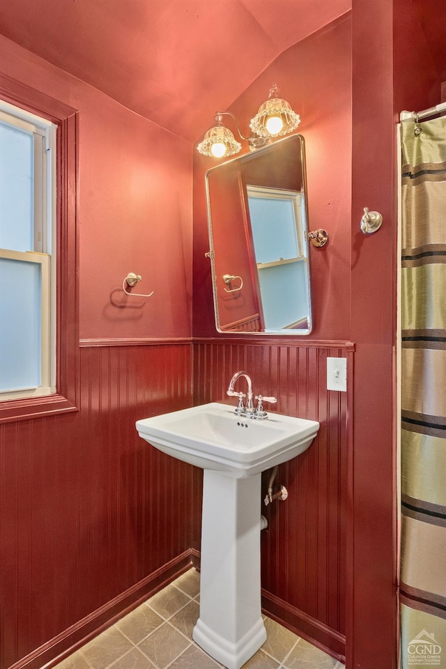 bathroom with wooden walls, tile patterned floors, lofted ceiling, and sink