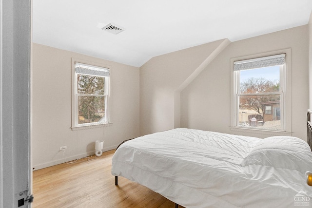 bedroom with multiple windows, visible vents, light wood-style floors, and lofted ceiling
