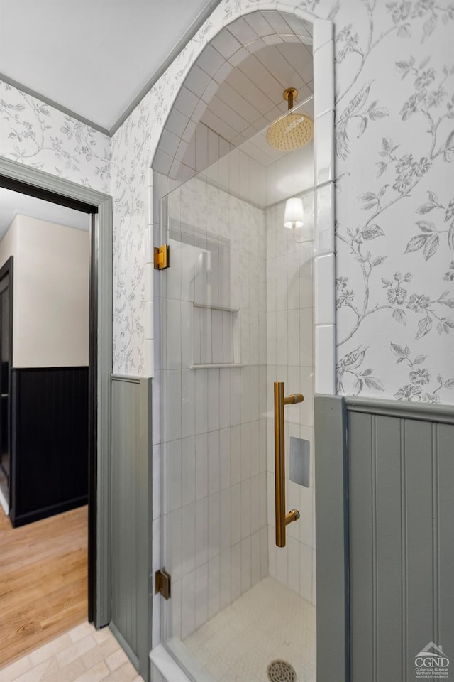 bathroom featuring wallpapered walls, a stall shower, and wainscoting