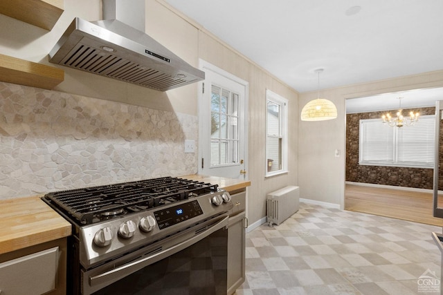 kitchen featuring radiator, hanging light fixtures, stainless steel gas range, wall chimney exhaust hood, and butcher block counters