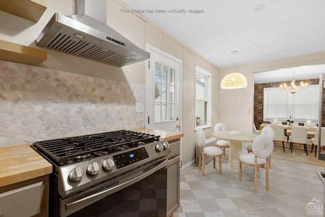 kitchen featuring wall chimney range hood, hanging light fixtures, a notable chandelier, gas stove, and butcher block counters