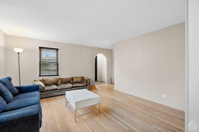 living area featuring arched walkways, baseboards, and light wood-style flooring