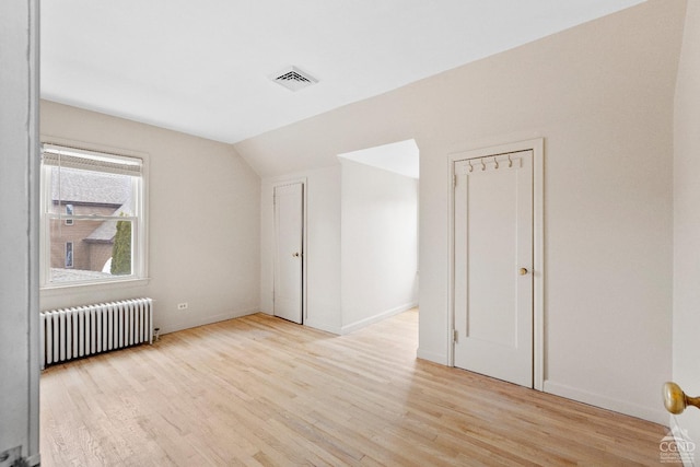 empty room with radiator, light wood-style floors, vaulted ceiling, and visible vents