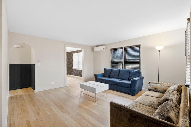 living room with baseboards, arched walkways, an AC wall unit, and light wood-style floors