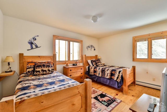 bedroom with multiple windows, light hardwood / wood-style floors, and a baseboard heating unit