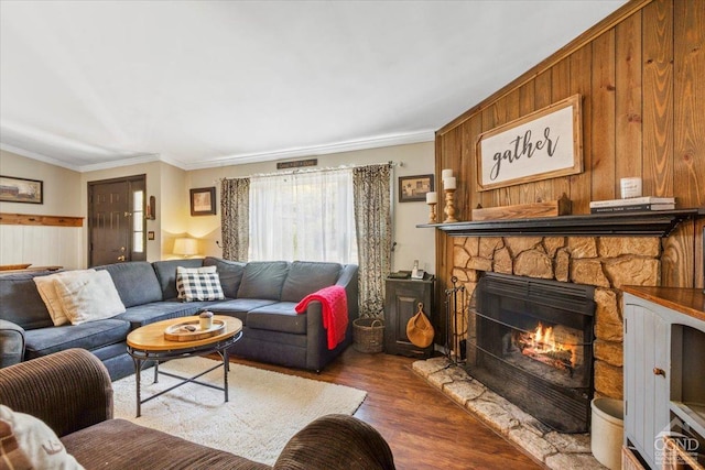 living area featuring a stone fireplace, wood finished floors, crown molding, and wood walls