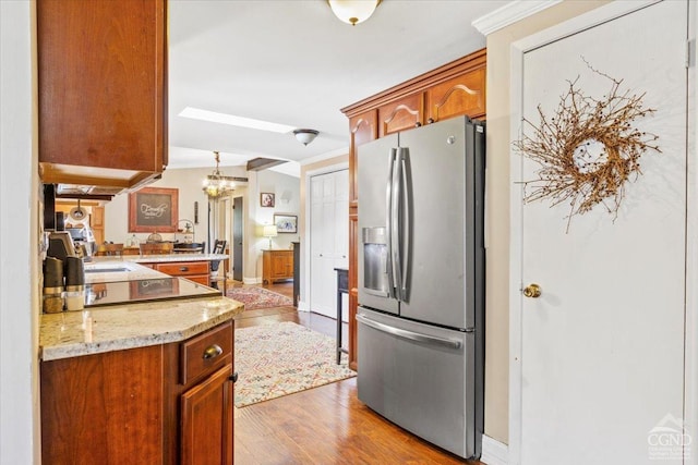 kitchen with light wood-type flooring, brown cabinets, a notable chandelier, stainless steel refrigerator with ice dispenser, and light stone countertops