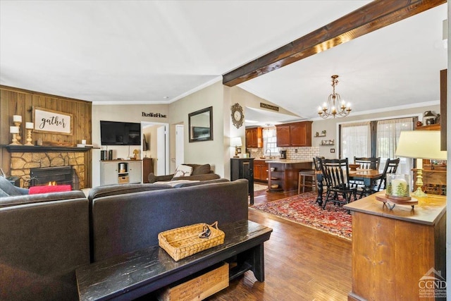 living room featuring a notable chandelier, ornamental molding, dark wood finished floors, a fireplace, and vaulted ceiling with beams