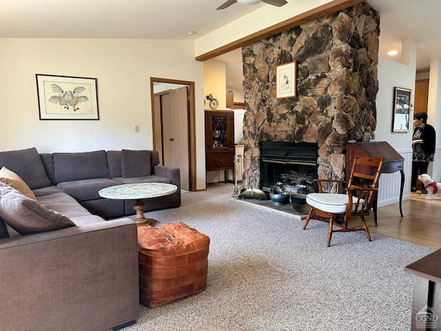 living area with lofted ceiling with beams, a stone fireplace, and ceiling fan