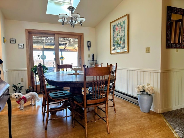 dining space with a notable chandelier, light wood-style floors, baseboard heating, and wainscoting