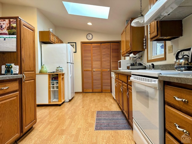 kitchen with under cabinet range hood, white appliances, vaulted ceiling with skylight, and brown cabinetry