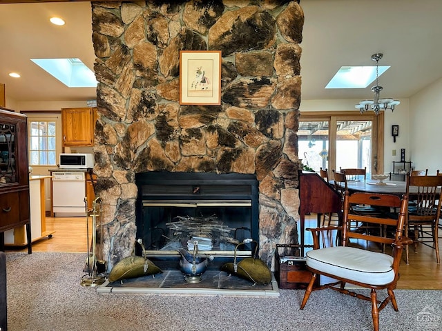 living area featuring a stone fireplace, lofted ceiling with skylight, light wood-type flooring, and a chandelier