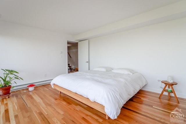 bedroom with a baseboard heating unit, light wood-style floors, and baseboards