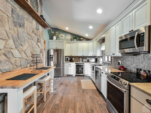 kitchen featuring dark wood-type flooring, vaulted ceiling, appliances with stainless steel finishes, tasteful backsplash, and beverage cooler