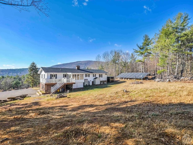 rear view of property featuring a wooden deck and solar panels