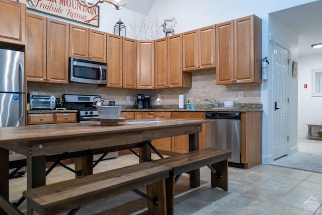 kitchen featuring lofted ceiling, dark stone counters, decorative backsplash, light tile patterned floors, and appliances with stainless steel finishes