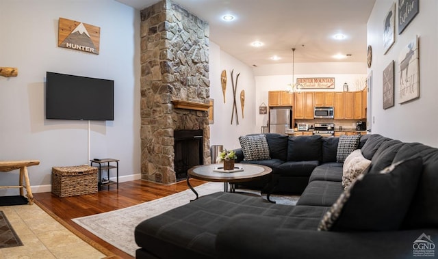 living room with a chandelier, light hardwood / wood-style floors, and a stone fireplace