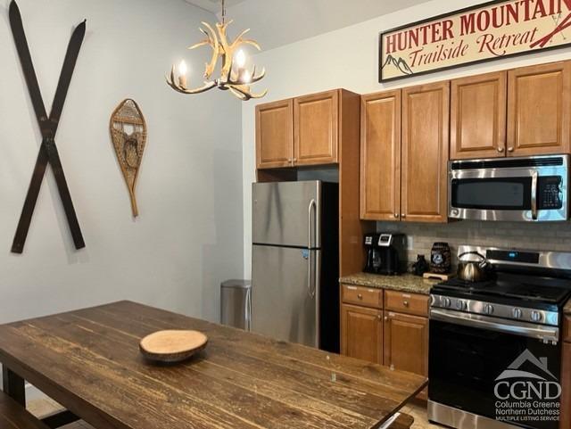 kitchen with tasteful backsplash, dark stone counters, stainless steel appliances, pendant lighting, and a chandelier