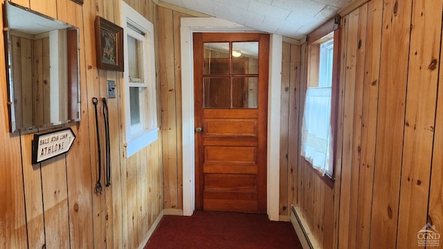 corridor with wooden walls, dark carpet, and a baseboard heating unit