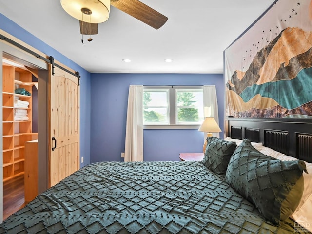 bedroom featuring wood-type flooring, a barn door, and ceiling fan