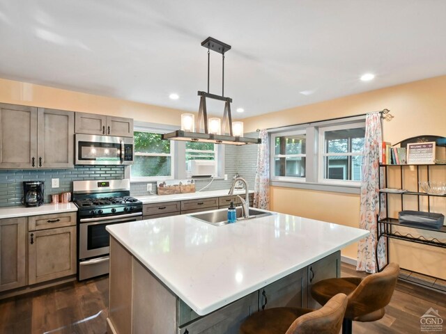 kitchen featuring a center island with sink, hanging light fixtures, sink, and appliances with stainless steel finishes