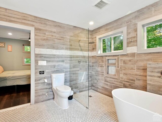 bathroom with tile patterned floors, ceiling fan, tile walls, shower with separate bathtub, and toilet