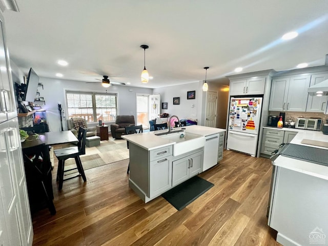 kitchen with white appliances, pendant lighting, a kitchen island with sink, ceiling fan, and sink