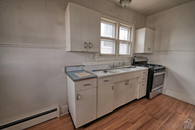 kitchen featuring a baseboard heating unit, white cabinets, stainless steel gas range, tile walls, and light hardwood / wood-style floors