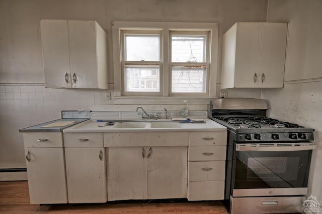 kitchen with white cabinets, sink, hardwood / wood-style flooring, a baseboard radiator, and stainless steel range with gas stovetop